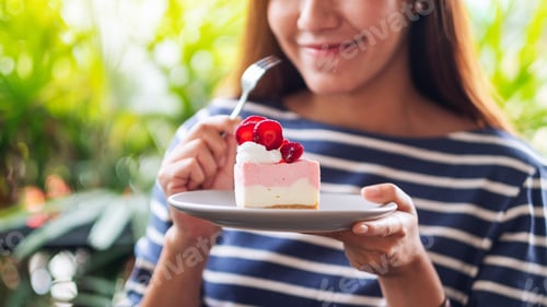 Preview: Closeup image of a beautiful young asian woman holding and eating a piece of strawberry cheese cake
