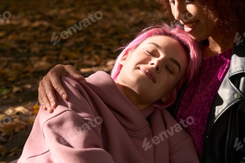 Preview: Mixed-race lesbian couple resting in park in sunny weather