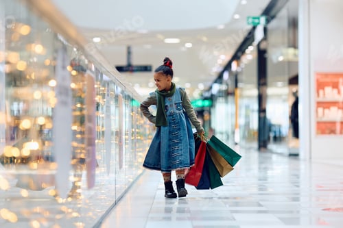 Preview: Happy black girl with shopping bags walking alone through the mall.