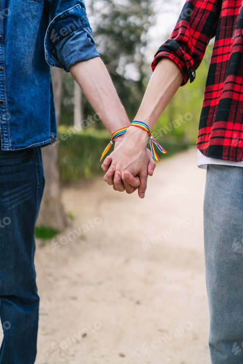 Preview: Close-up of Male Couple Holding Hands with Multicolor LGBT Bracelets Outdoors