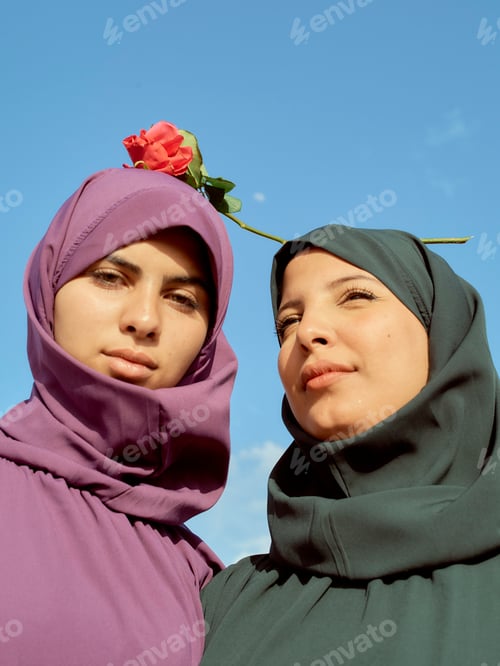 Preview: Two women wearing colorful hijabs pose with a rose against a clear blue sky, Morocco