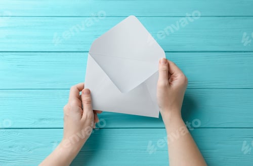Preview: Woman with white paper envelope at light blue wooden table, top view