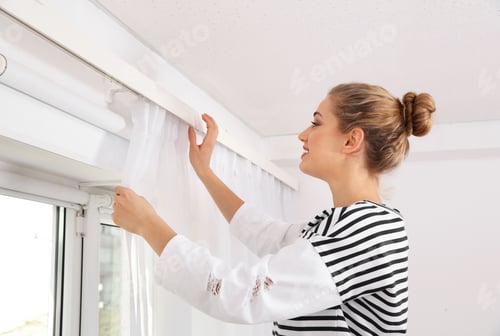 Preview: Woman hanging window curtain indoors. Interior decor element