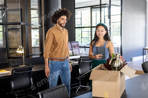 Preview: Colleagues discussing office relocation while unpacking box in modern workspace