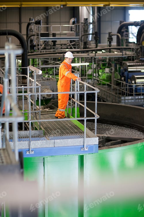 Preview: Worker in orange safety gear inspecting industrial equipment.