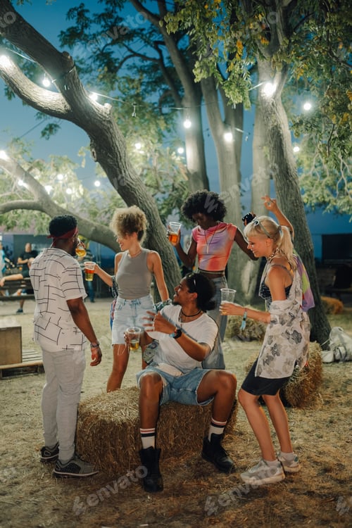 Preview: Friends enjoying drinks and dancing at a summer music festival under string lights