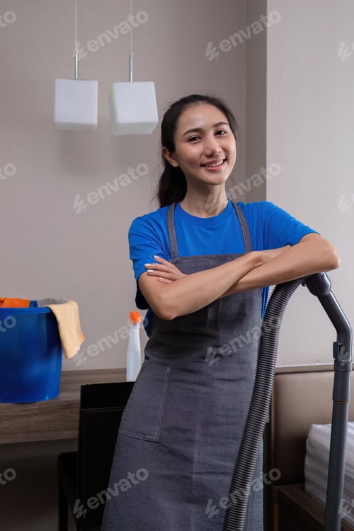 Preview: A young female cleaner stands with a vacuum cleaner while vacuuming the bedroom
