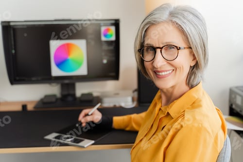 Preview: Portrait smiling senior woman, graphic designer, editor, retoucher sitting at workplace