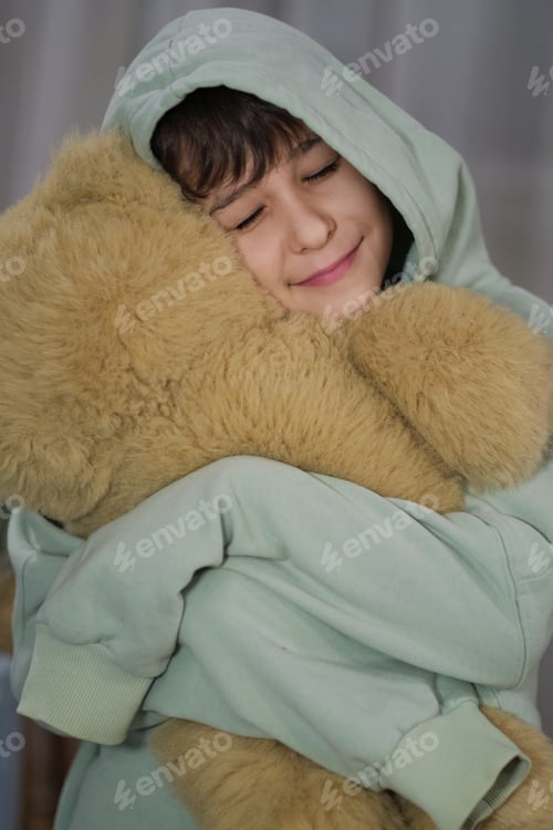 Preview: A young boy in a hooded sweater, embracing a soft teddy bear with a peaceful expression.