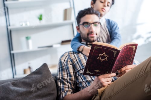 Preview: selective focus of jewish father and son reading tanakh in apartment