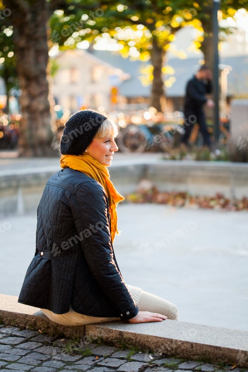 Preview: Happy woman sitting on retaining wall at park