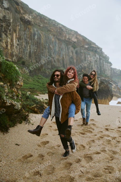 Preview: Two young adult couples walking on beach together in cloudy weather