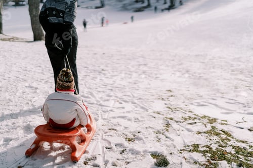 Preview: Mom carries a small child on a sled across a snowy plain. Back view. Cropped