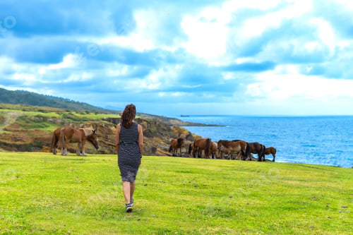 Preview: Woman walking towards horses grazing near atlantic ocean