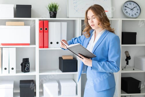 Preview: A beautiful young girl stands near a rack in the office and holds an open book in her hands.