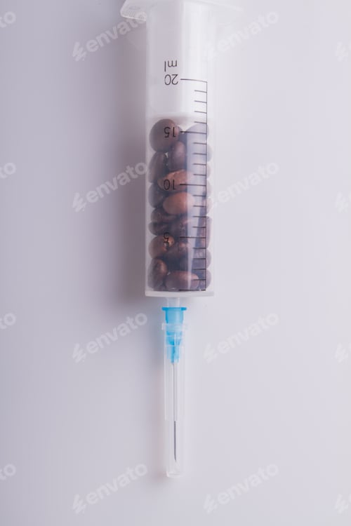 Preview: Medical syringe full of coffee beans over white background.