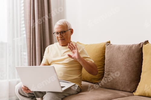 Preview: Senior man waving into camera on laptop during online meeting