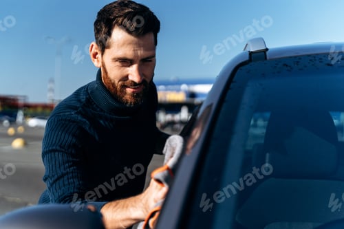 Preview: Handsome caucasian man washing and wiping his car with pleasure smile