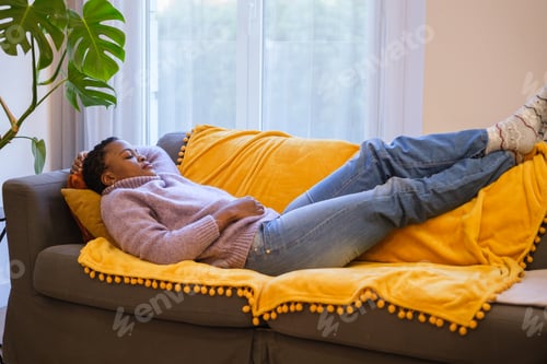 Preview: Young woman with short curly hair napping on the sofa in her living room. Concept: rest, nap, sleep
