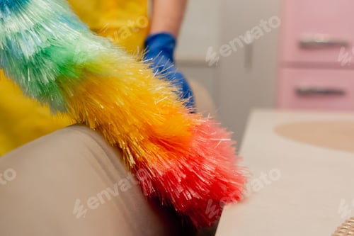 Preview: close up in the apartment cleaner in a yellow apron is cleaning chairs with a dust brush