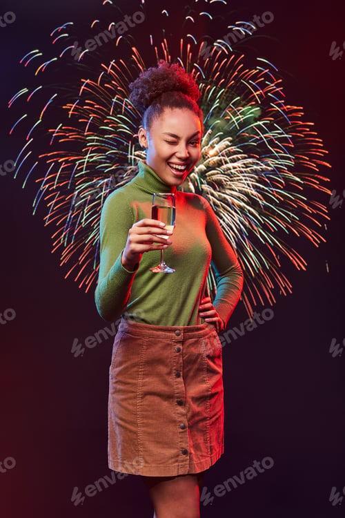 Preview: Happy New Year. Young beautiful mixed race woman holding glass of champagne and winking while