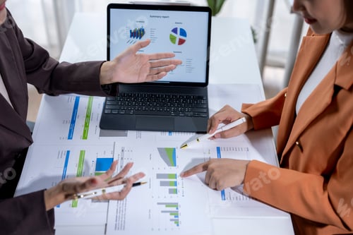 Preview: Businesswomen analyzing financial charts on paperwork and digital tablet during a meeting