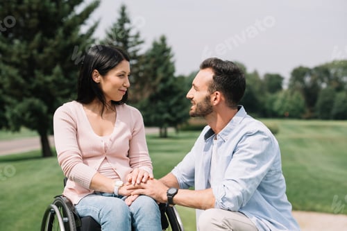 Preview: happy handsome man looking at smiling disabled girlfriend in park