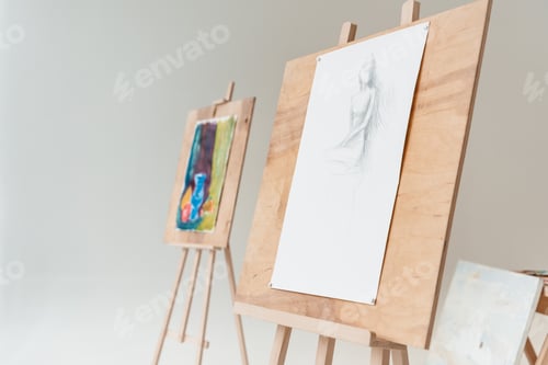 Preview: easels with artistic paintings in empty art studio on grey