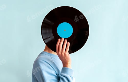 Preview: Man in blue sweatshirt covers his face with vinyl record on blue background
