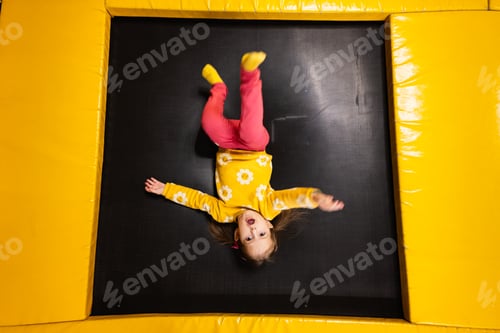 Preview: Baby girl kid lies upside down on trampoline at playground park.