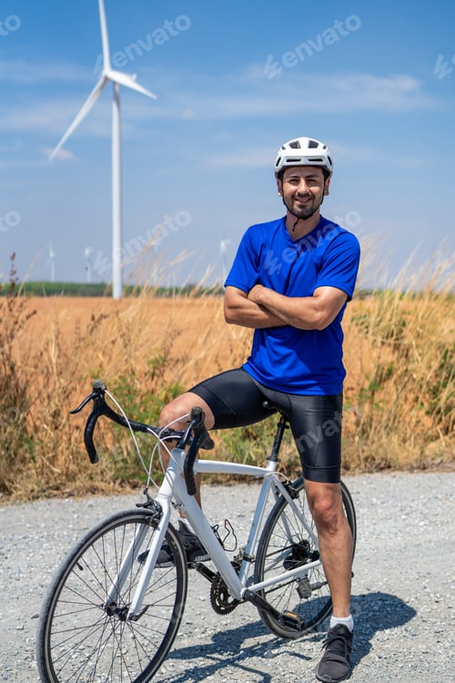 Preview: Portrait of Caucasian sportsman riding bicycle at wind turbine field.