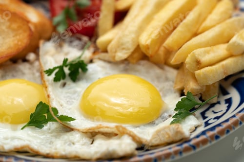 Preview: Breakfast plate with fried eggs, sausage, tomatoes, and fries served on a decorative blue plate