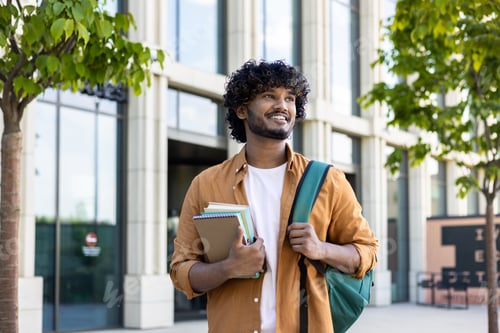 Preview: Portrait of young Indian male student, applicant standing outside campus, holding books and