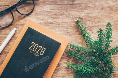 Preview: Cozy Workspace With 2026 Planner, Eyeglasses, Pen and Fir Tree Branch on Wooden Desk. Flat lay
