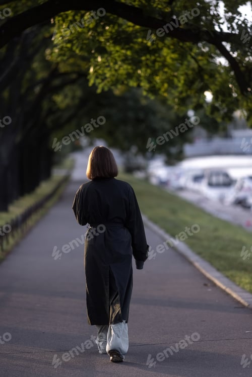 Preview: Back view of slender young woman wearing hat and coat walking down street