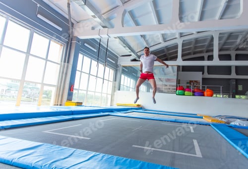 Preview: Fitness, fun, leisure and sport activity concept - Handsome happy man jumping on a trampoline