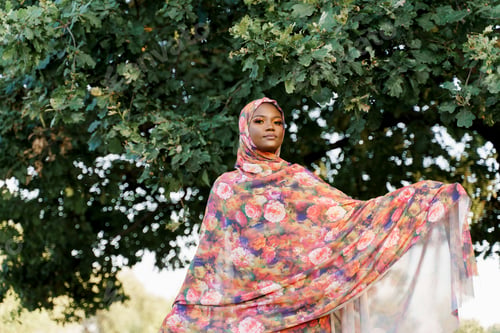 Preview: Attractive black Muslim girl in hijab smiling near tree, modern African lifestyle