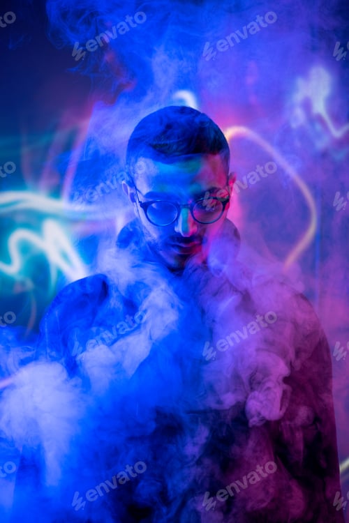 Preview: Head of young man in eyeglasses standing in smoke and blue neon light