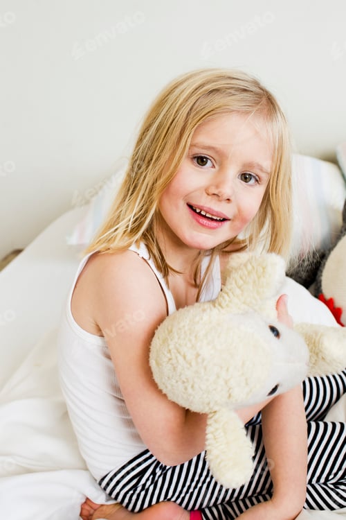 Preview: Portrait of young girl kneeling on bed with soft toy