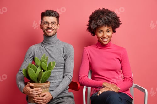Preview: Horizontal shot of mixed race young woman and man sit on comfortable chairs have happy expressions s