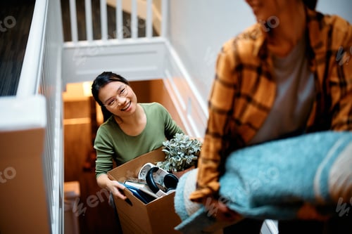 Preview: Happy Asian woman and her friend carrying their stuff upstairs while relocating into new apartment.