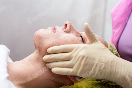 Preview: Beautician cleans the woman face with massaging movements using a scrub