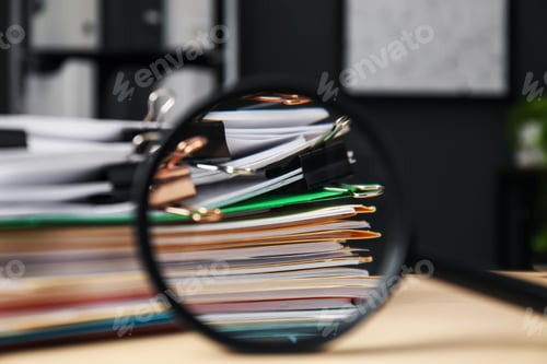 Preview: Magnifying glass, many folders with documents and binder clips on wooden desk, closeup