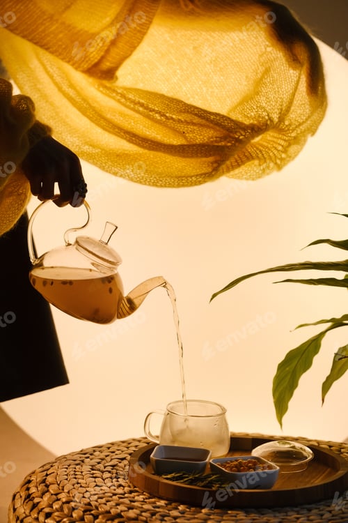 Preview: Close-up of a hand with a kettle. A teapot with sea buckthorn tea, honey and a plate with sea