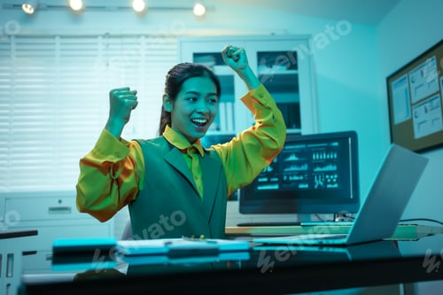 Preview: Asian businesswoman celebrating success at her desk, delighted after achieving business goals