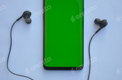 Preview: High angle shot of smartphone phone with green screen and black color earphone