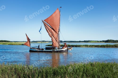 Preview: Traditional sailing boat with red sails and a gaff rig, a sailing smack on the water on a reed bed