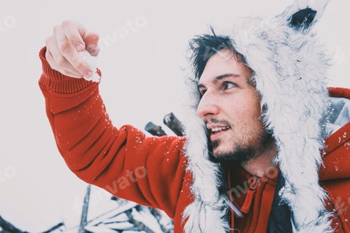 Preview: Young man enjoying a snowy day wearing a fur hat and a red hoodie