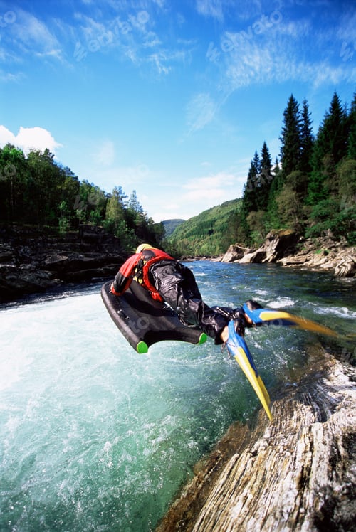 Preview: Young woman in wetsuit jumping from cliff into river