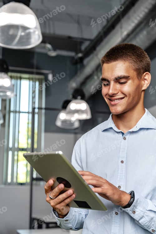 Preview: Young handsome businessman using digital tablet while standing in the office